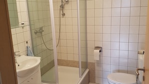Een badkamer met een douchecabine, een wastafel, een toilet en twee blauwe matten op de vloer.