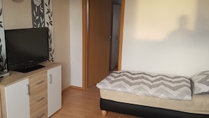 Een slaapkamer met een bed, een televisie, een kledingkast en een deur naar een andere kamer.