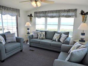 A living room with a grey sofa set, patterned throw pillows, a small side table with a lamp, and a ceiling fan.