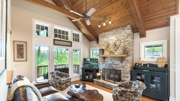 Una sala de estar acogedora con chimenea de piedra, sofá de cuero, sillones estampados y televisor.
