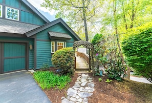 A house with a stone pathway leading to a wooden archway, a covered porch.