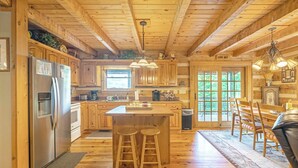 Une cabane en bois dotée d’une cuisine comprenant un réfrigérateur, des placards en bois, un coin bar avec des tabourets et une table à manger avec des chaises.