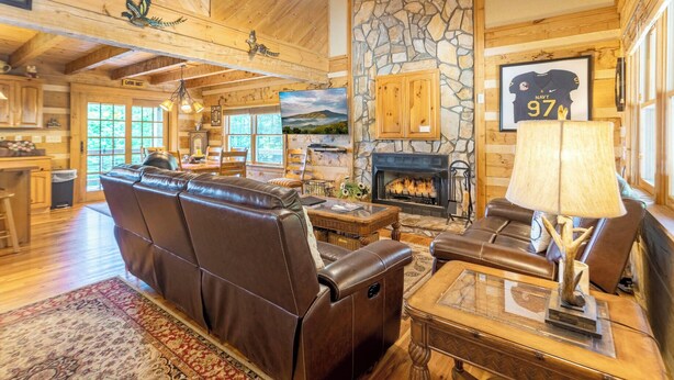 Un intérieur de chalet chaleureux avec une cheminée en pierre, des fauteuils en cuir et un coin repas.