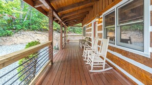 Une terrasse en bois, dotée de fauteuils à bascule et d’une balustrade, qui offre une vue sur un paysage naturel.