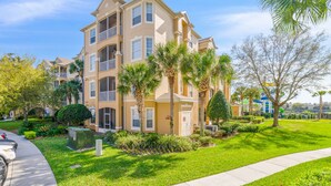 A multi-story residential building with balconies, surrounded by well-maintained lawns and palm trees.