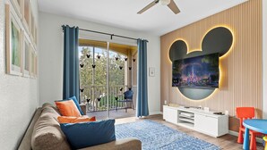 A modern living room with a sofa, a TV mounted on a wall, a balcony with a view, and a ceiling fan.