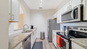 A modern kitchen with white cabinets, stainless steel appliances, a microwave, oven, and a sink.