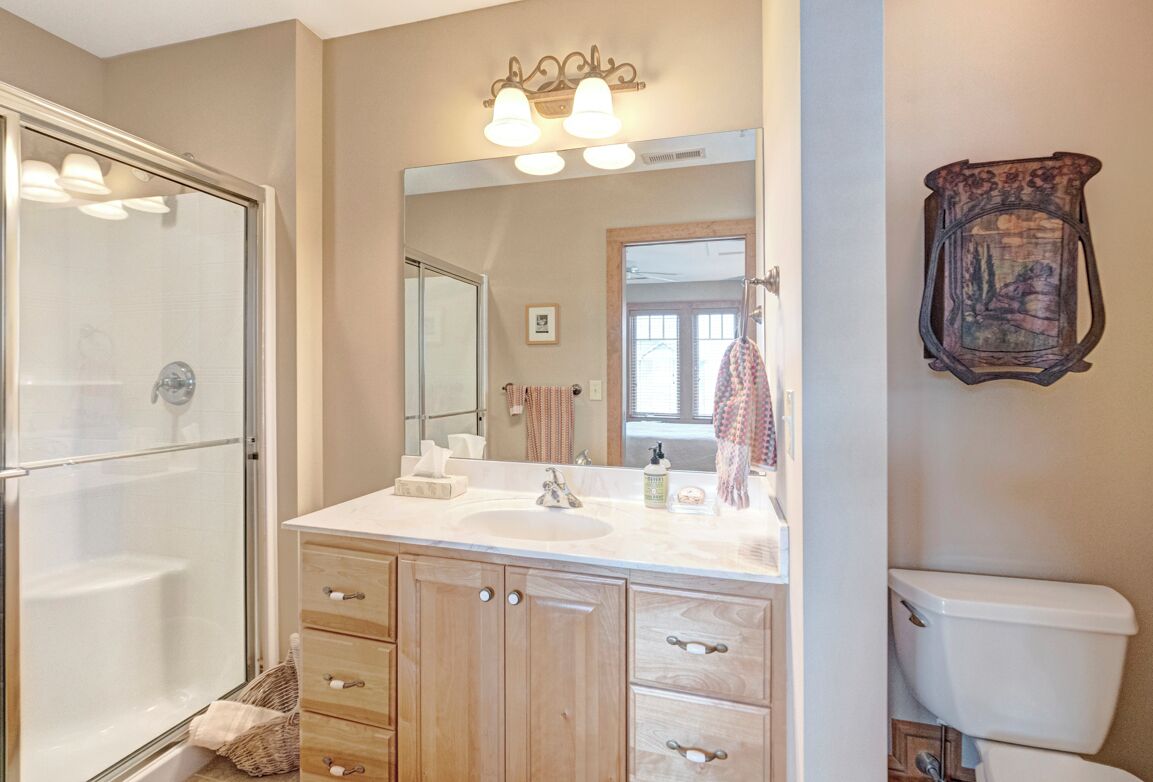 A bathroom with a glass shower enclosure, a sink with a mirror above it, wooden cabinets, and a toilet.