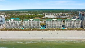 Hotel ved stranden med flere høje bygninger, en sandstrand og et fjerntliggende bybillede.