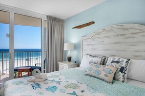 A bedroom with a bed, a nightstand, a lamp, a view of the beach, and a chair. - Oceanfront escape! Relax in this cozy 1BR condo at Panama City Beach. FREE BEACH CHAIRS! (Panama City Beach)