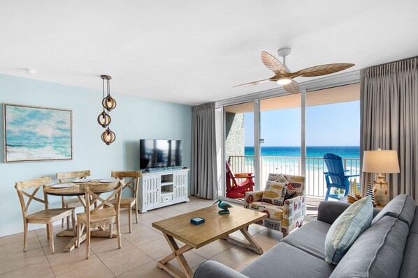 A living room with a TV, wooden furniture, a balcony with a view of the ocean, and a ceiling fan. - Oceanfront escape! Relax in this cozy 1BR condo at Panama City Beach. FREE BEACH CHAIRS! (Panama City Beach)