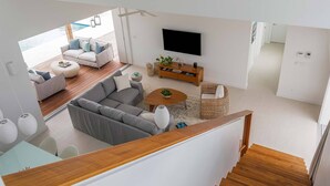 A modern living room with a grey sofa, a round coffee table, and a flat-screen TV on the wall. - Aqueous: Luxury Villa w/Tranquil Pool Near Beach (Leeward Settlement)