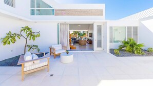 A modern outdoor living area with a sofa, coffee table, and plants. - Aqueous: Luxury Villa w/Tranquil Pool Near Beach (Leeward Settlement)