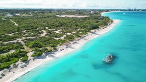 An aerial view of a coastal area with a sandy beach, clear turquoise waters, and a small boat anchored near the shore. - Aqueous: Luxury Villa w/Tranquil Pool Near Beach (Leeward Settlement)