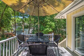 A covered outdoor patio with a table and chairs, surrounded by a white railing and trees.