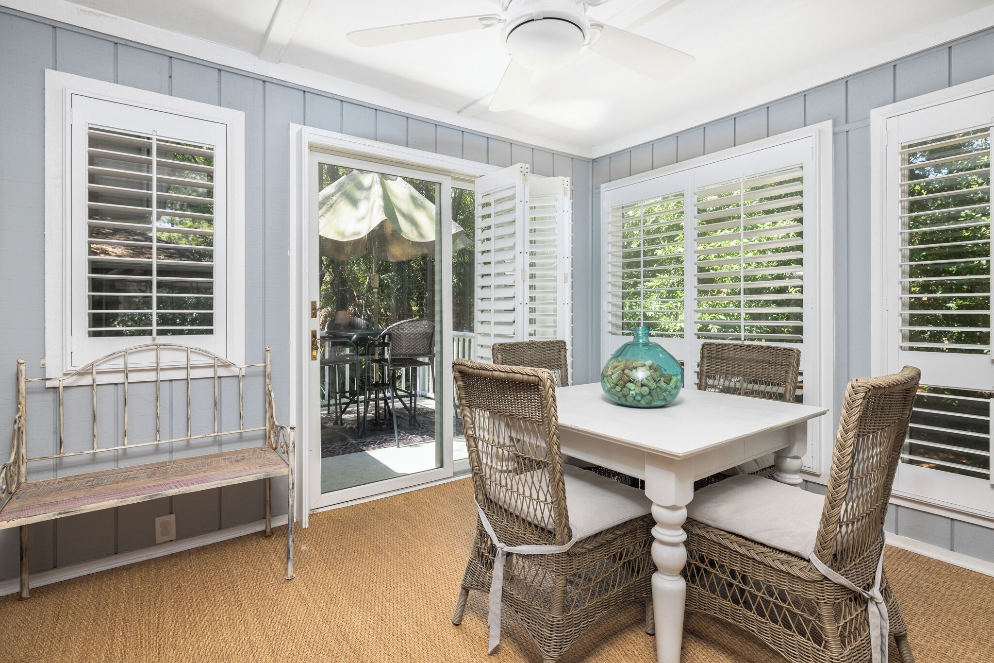 A dining area with wicker chairs, a white table, and a ceiling fan.