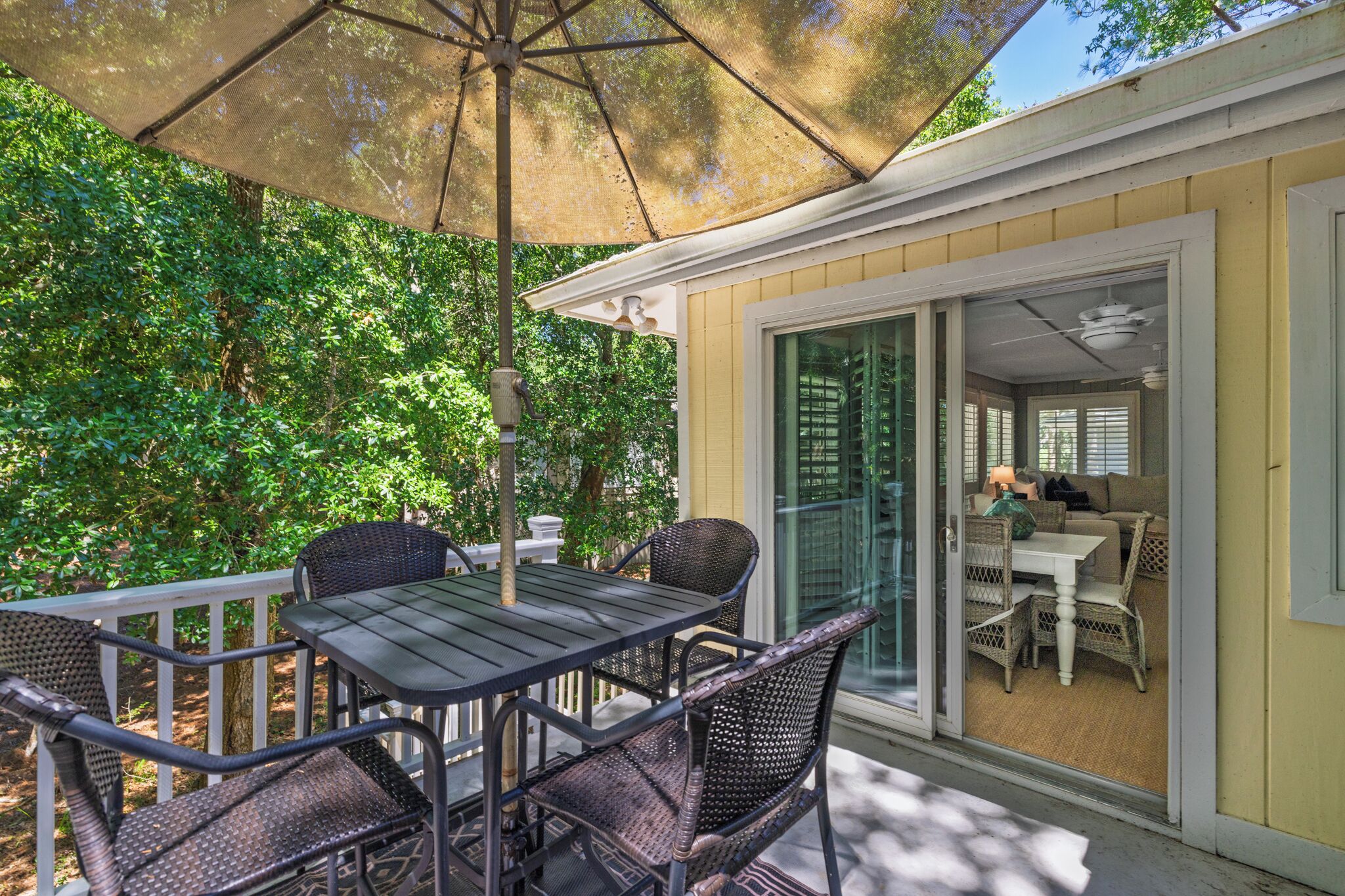 A patio with a table and chairs, an umbrella, and a view of a room with a couch and table.