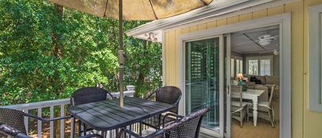 A patio with a table and chairs, an umbrella, and a view of a room with a couch and table.