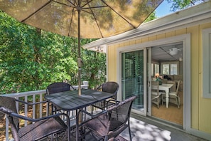 Een terras met een tafel, stoelen en een parasol, en uitzicht op een kamer met een bank en tafel.