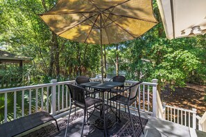 A covered outdoor seating area with a table and chairs, surrounded by a white railing and lush greenery.