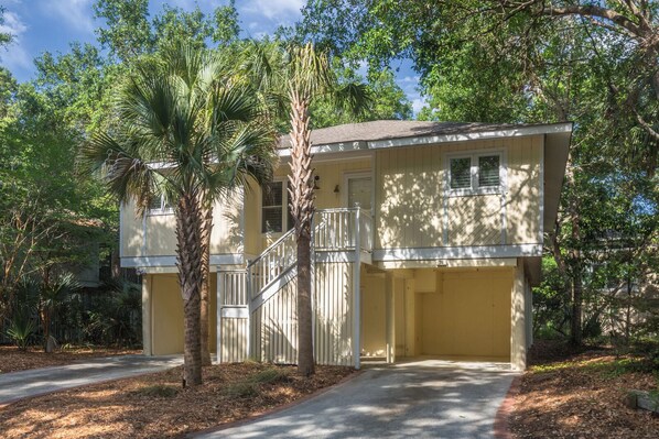A two-story yellow building with a covered porch, a staircase, and a gated entrance.