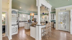 A spacious kitchen with white cabinetry, a central island, and a dining area with bar stools. - Sandy Shanty: Luxurious Beach House with Rooftop Ocean Views! (Isle of Palms)