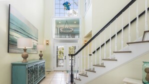 A staircase with a white railing, a teal cabinet with two lamps, and a chandelier. - Sandy Shanty: Luxurious Beach House with Rooftop Ocean Views! (Isle of Palms)