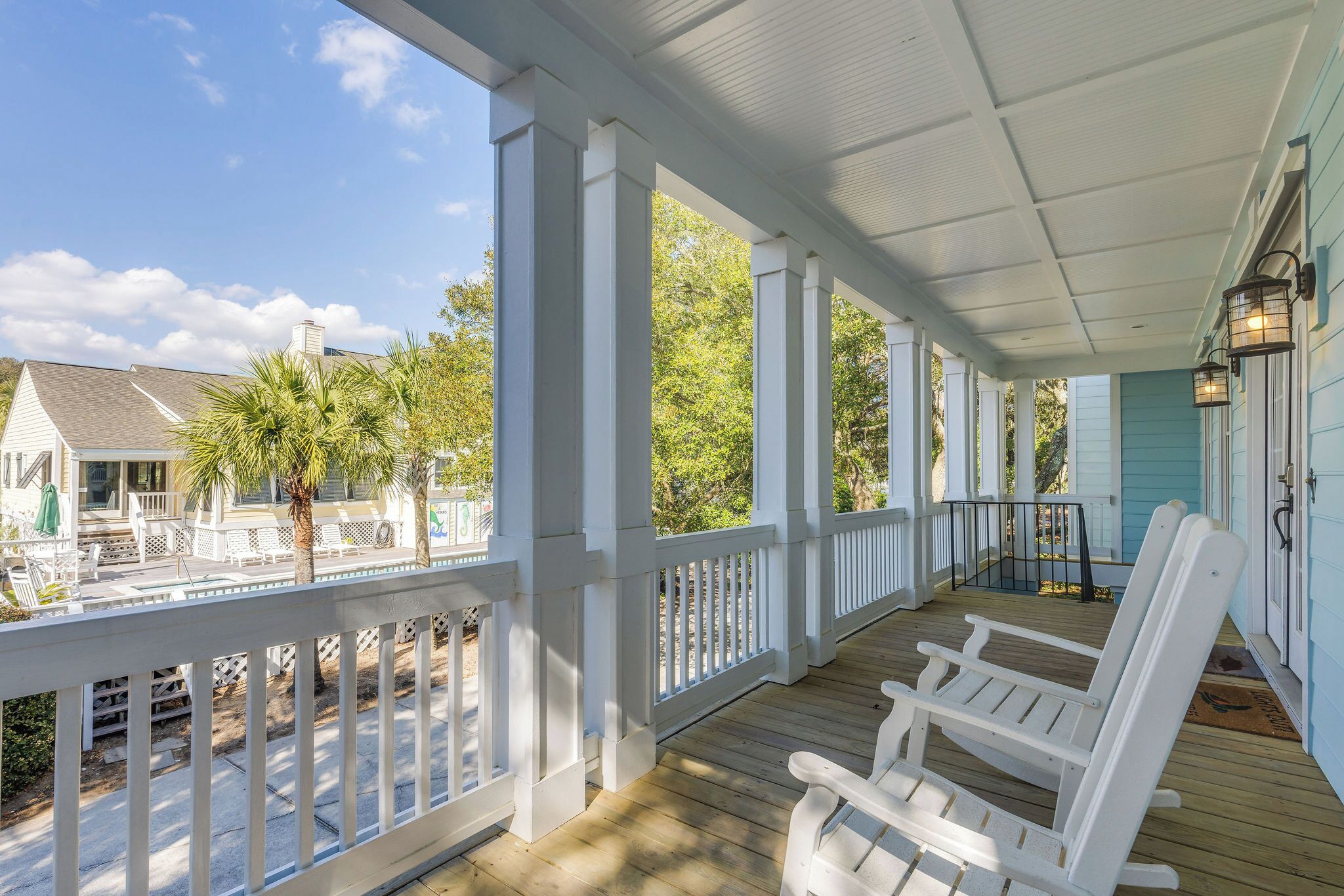 A covered porch with white railings, wooden flooring, and white Adirondack chairs.