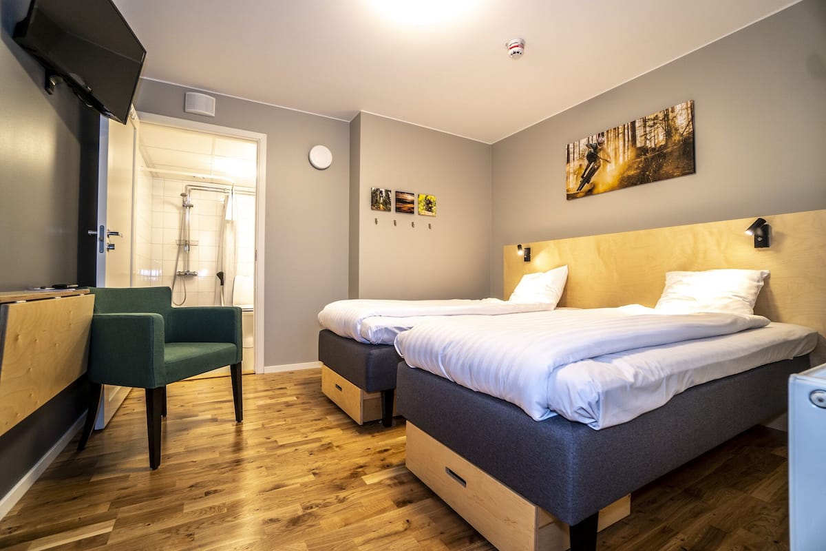 A hotel room with two beds, a desk, a chair, and a shower area.