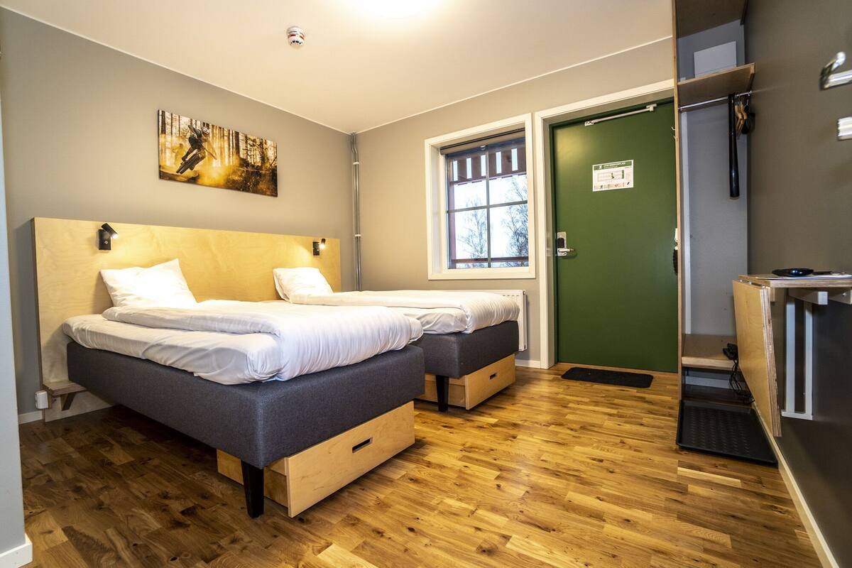 A bedroom with two beds, a wooden floor, a green door, and a window.