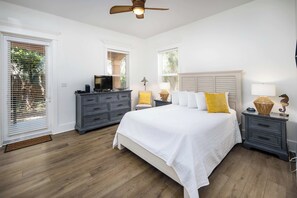 A bedroom with a bed, two bedside tables, a dresser, a ceiling fan, and windows with blinds.