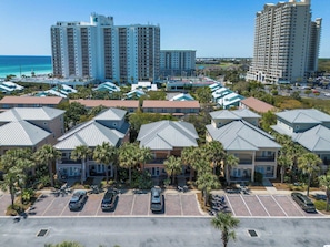 A hotel with multiple-story buildings, a parking lot, and a view of the ocean.