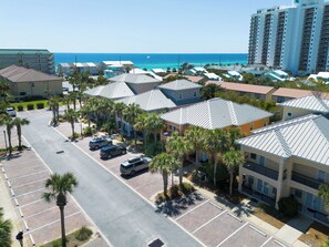 A coastal hotel with multiple-story buildings, a parking lot, and a view of the ocean.