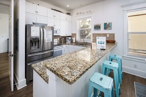 Una cocina moderna con armarios blancos, encimeras de granito, electrodomésticos de acero inoxidable y una isla grande con taburetes de bar.