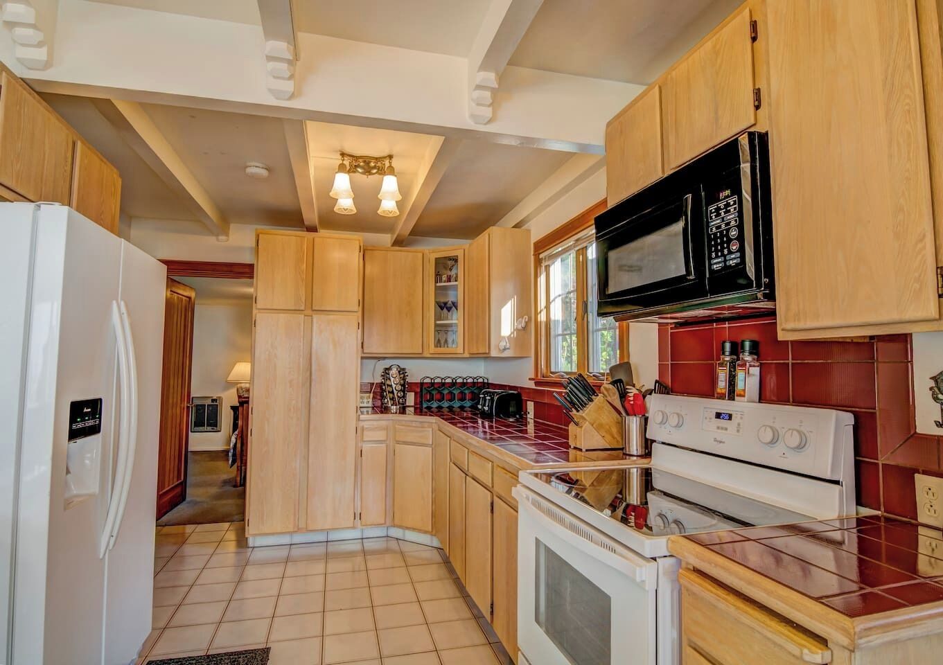 A kitchen with wooden cabinets, a refrigerator, a microwave, a stove, and a tiled backsplash.