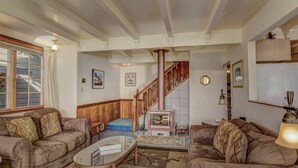 A living room with two sofas, a coffee table, a fireplace, a staircase, and a window with curtains.