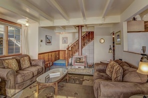 A living room with two sofas, a coffee table, a fireplace, a staircase, and a window with curtains. - Beach Treasure- Ocean view~ Oceanside (Oceanside)