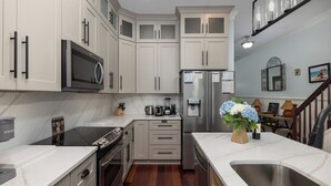 A kitchen with white cabinets, a stainless steel refrigerator, a microwave, a stove, and a sink.