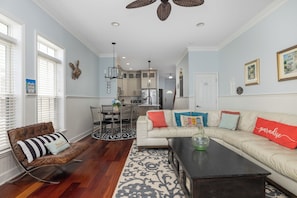 A living room with a sofa, coffee table, and a dining area with chairs and a table. - Charming 3BR Folly Beach Townhome: Water Views, Pool Access & Steps to Fun (Folly Beach)