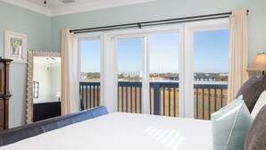 A bedroom with a large bed, a view of a balcony with a railing, and a window with curtains.