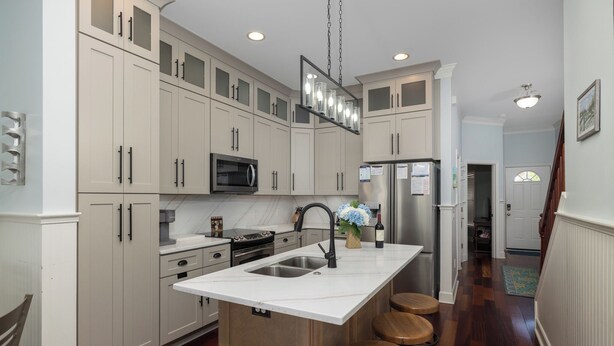 A kitchen with white cabinets, a central island with stools, a stainless steel refrigerator, and a microwave.