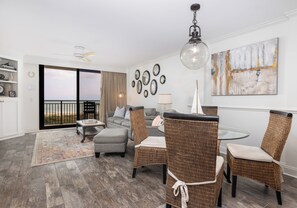 A modern living room with a balcony, grey sofas, wicker chairs, a glass table, and a large abstract painting.