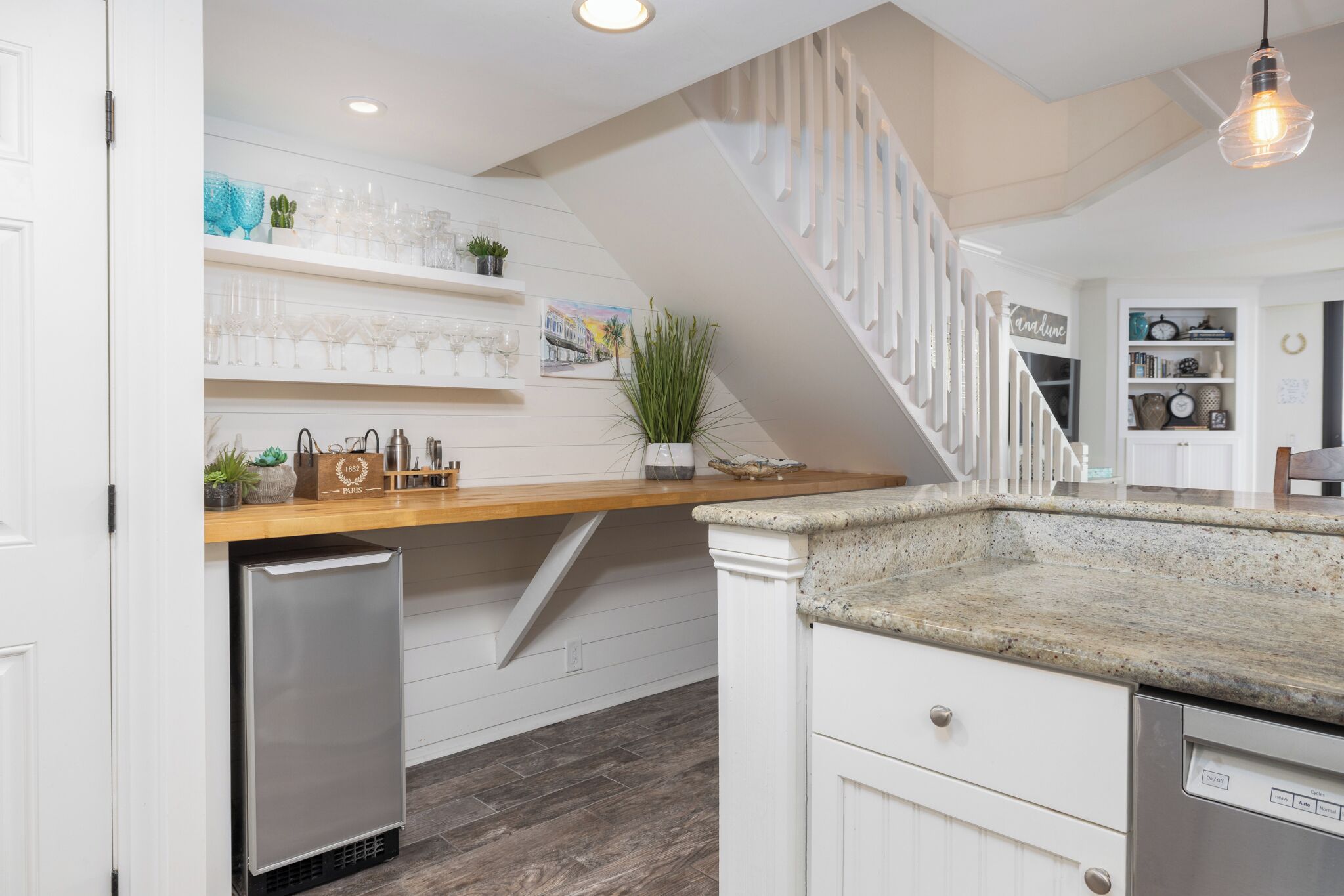 A kitchen with a wooden countertop, white cabinetry, a stainless steel dishwasher, and a staircase with white railings.