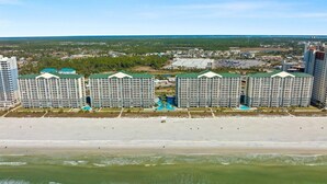 Et hotel ved stranden med flere høje bygninger, et poolområde og en strand i forgrunden.