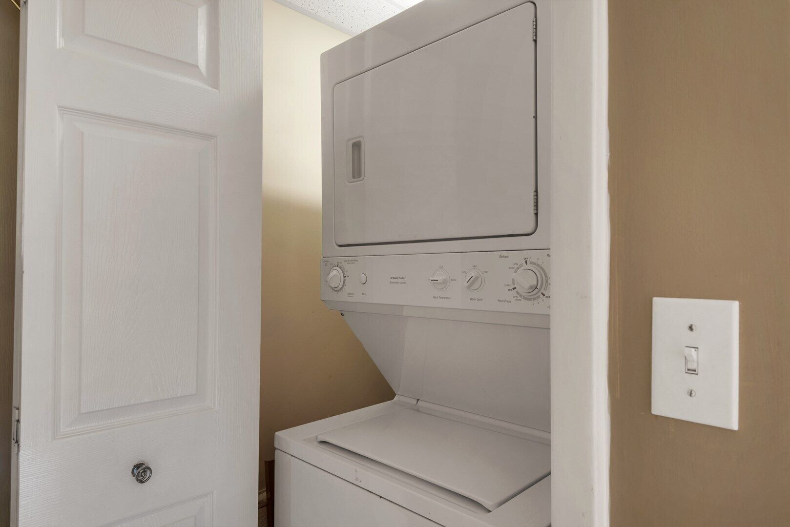 A laundry room with a front-loading washer and dryer, a door, and a light switch on the wall.