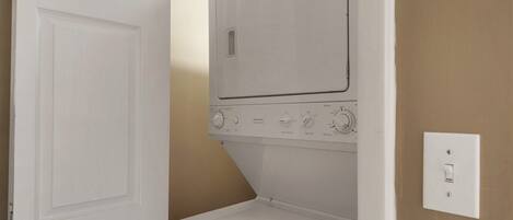 A laundry room with a front-loading washer and dryer, a door, and a light switch on the wall.