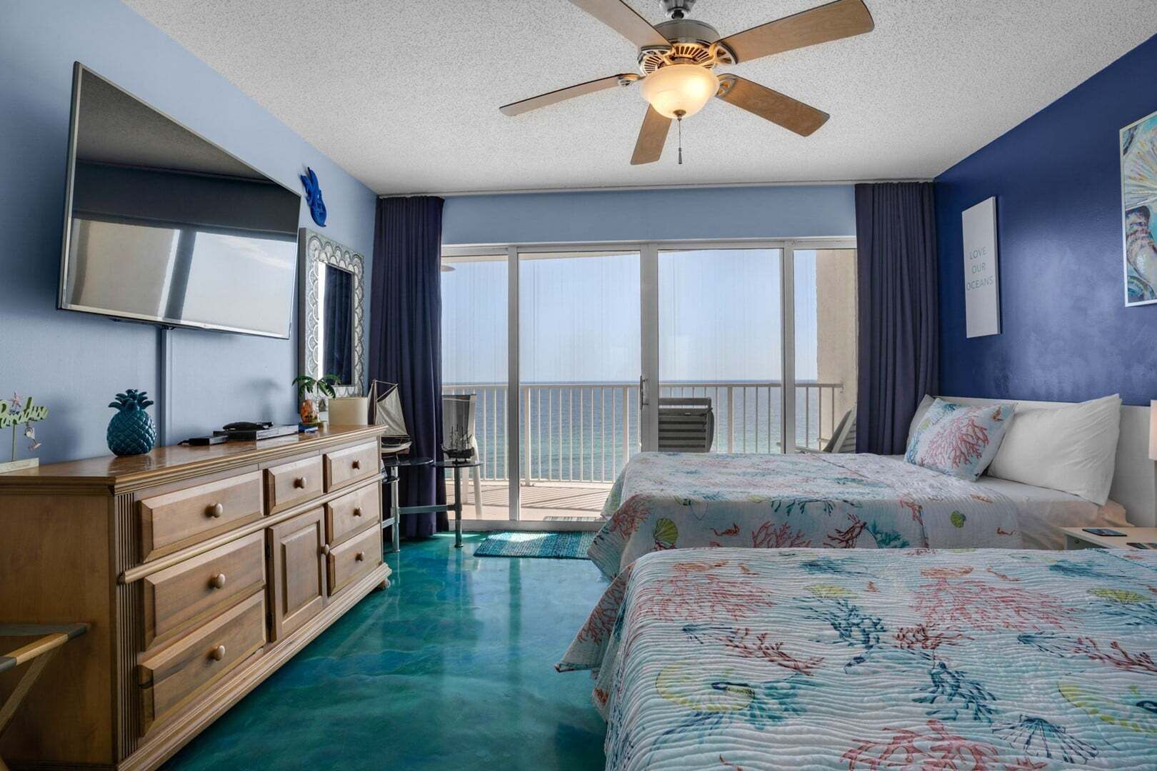 Une chambre à coucher avec un lit, une commode, un ventilateur de plafond et une vue sur l’océan.