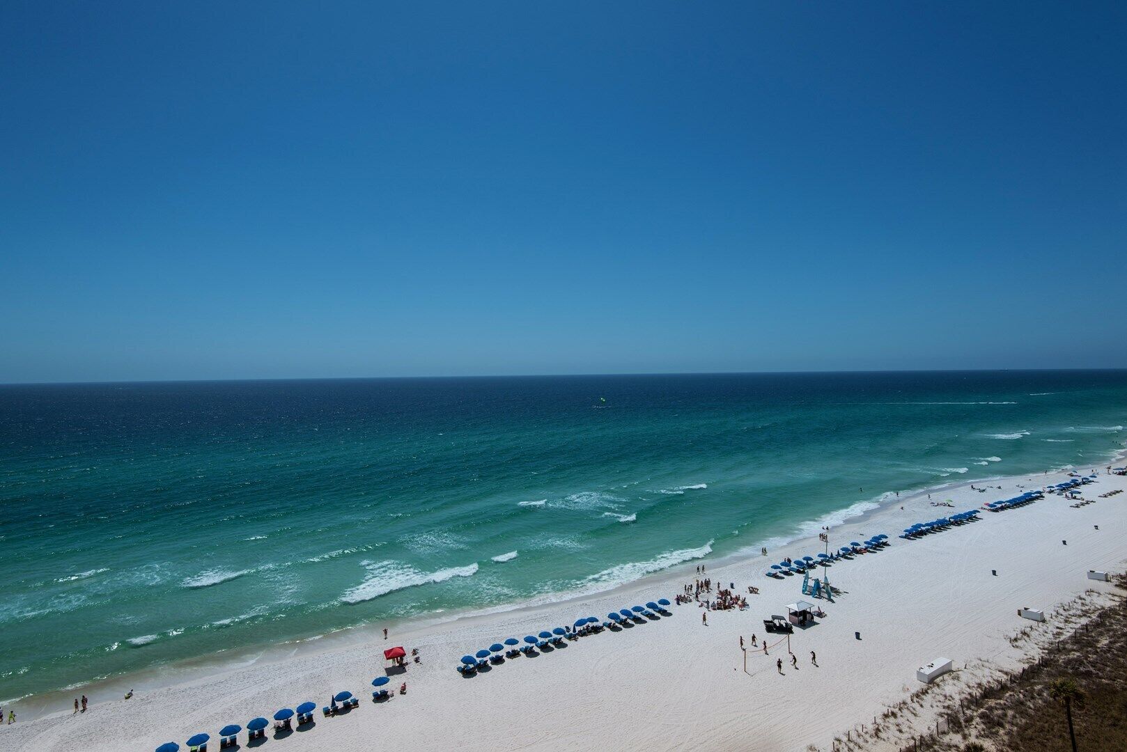 Ein Strand mit weißem Sand, klarem, blauem Wasser und einer Reihe blauer Sonnenschirme.