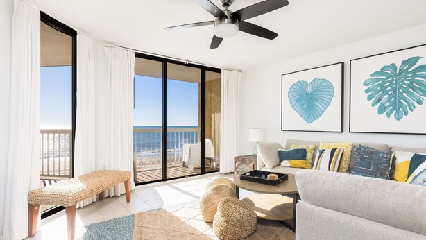 Un salon spacieux avec un balcon, un ventilateur de plafond et un canapé agrémenté de coussins colorés.