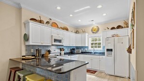 A kitchen with white cabinets, a central island, and colorful stools.